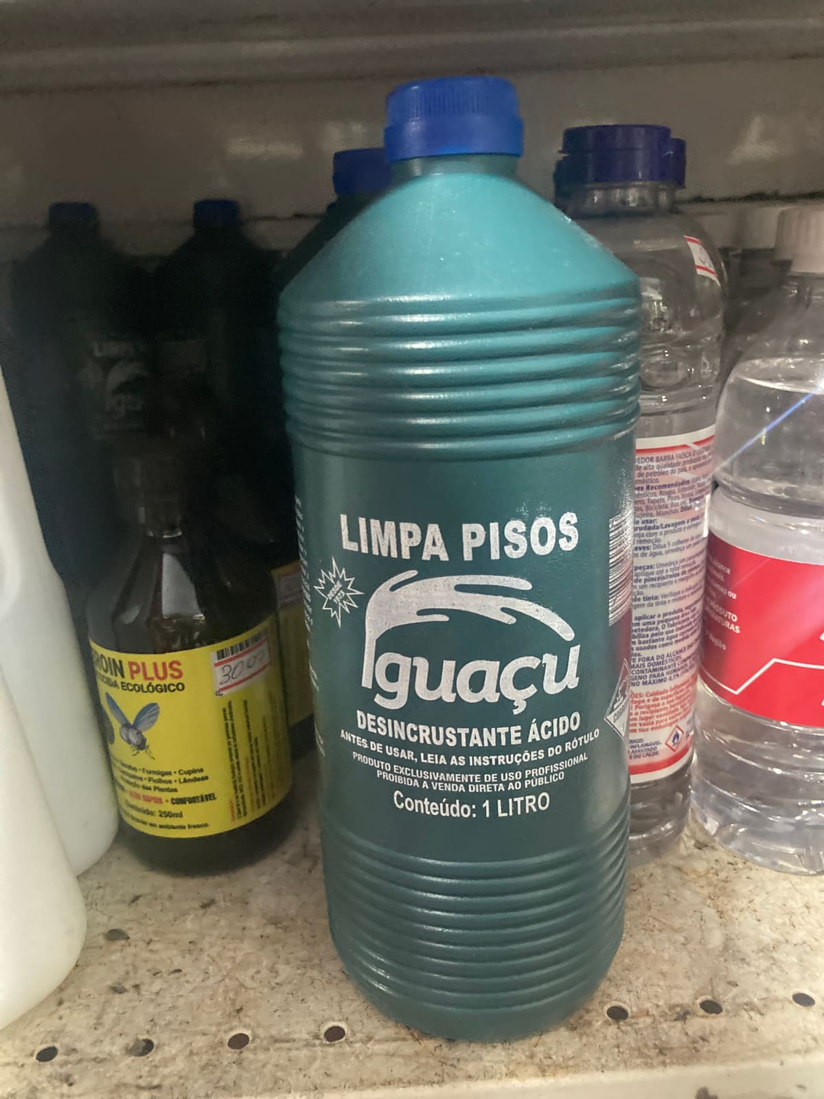 Garrafa plástica verde de Limpa Pisos Iguaçu de 1 litro em uma prateleira de loja ao lado de outros produtos.